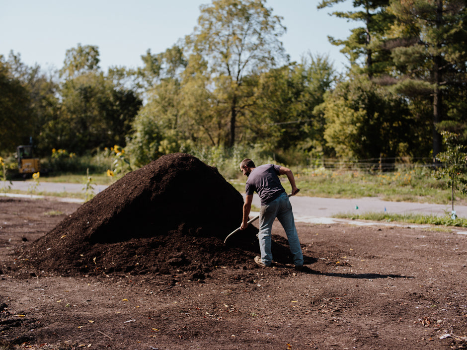 Person working with a large pile of compost in an outdoor setting