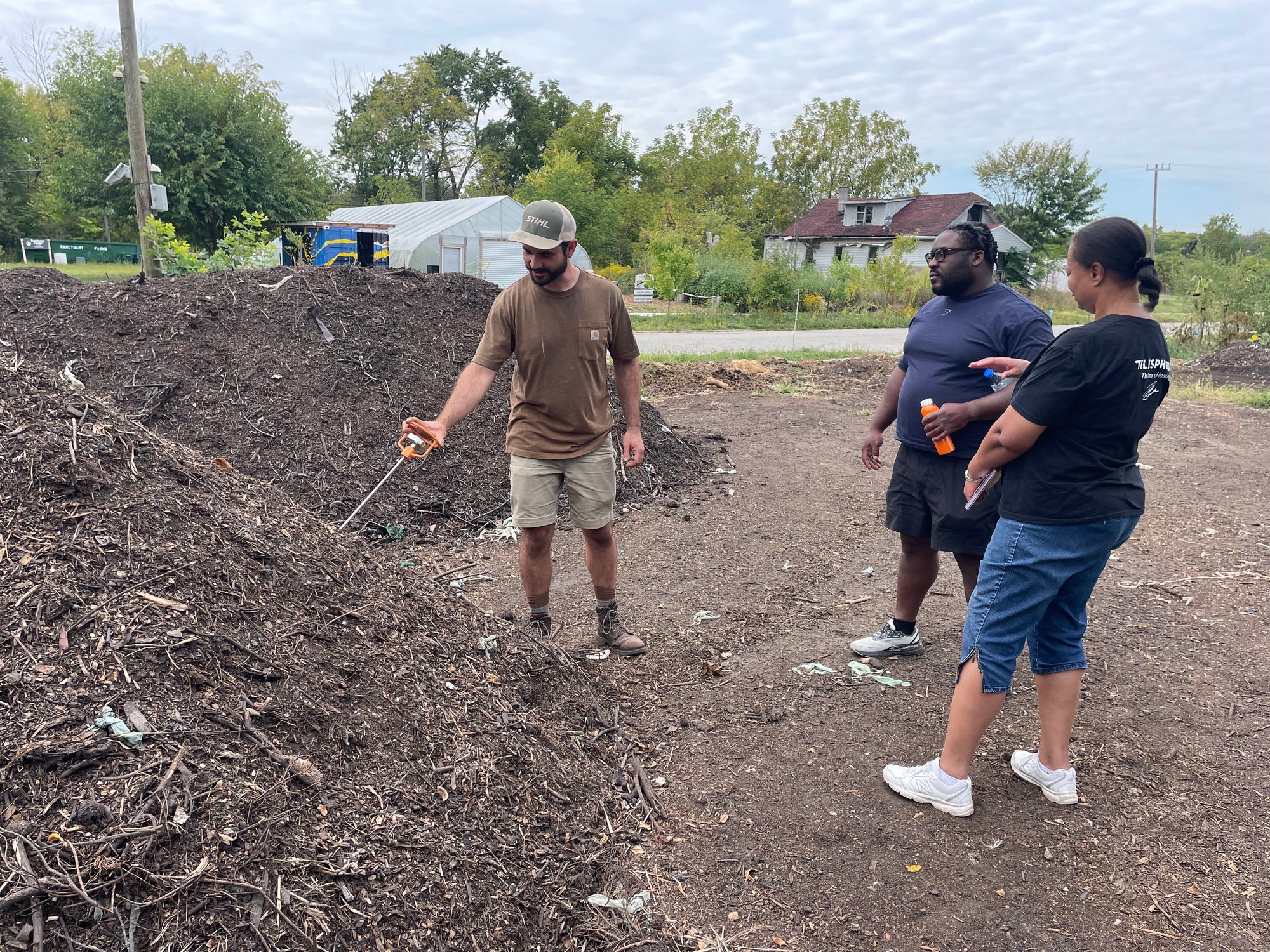 Three people standing checking the temperature of a compost pile