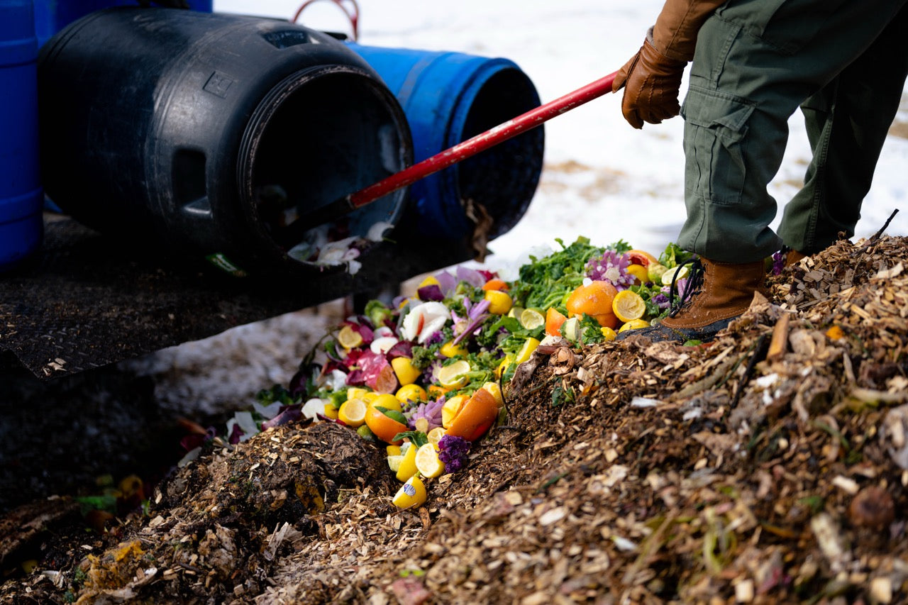 Person composting food waste into a pile with a blue bin nearby.