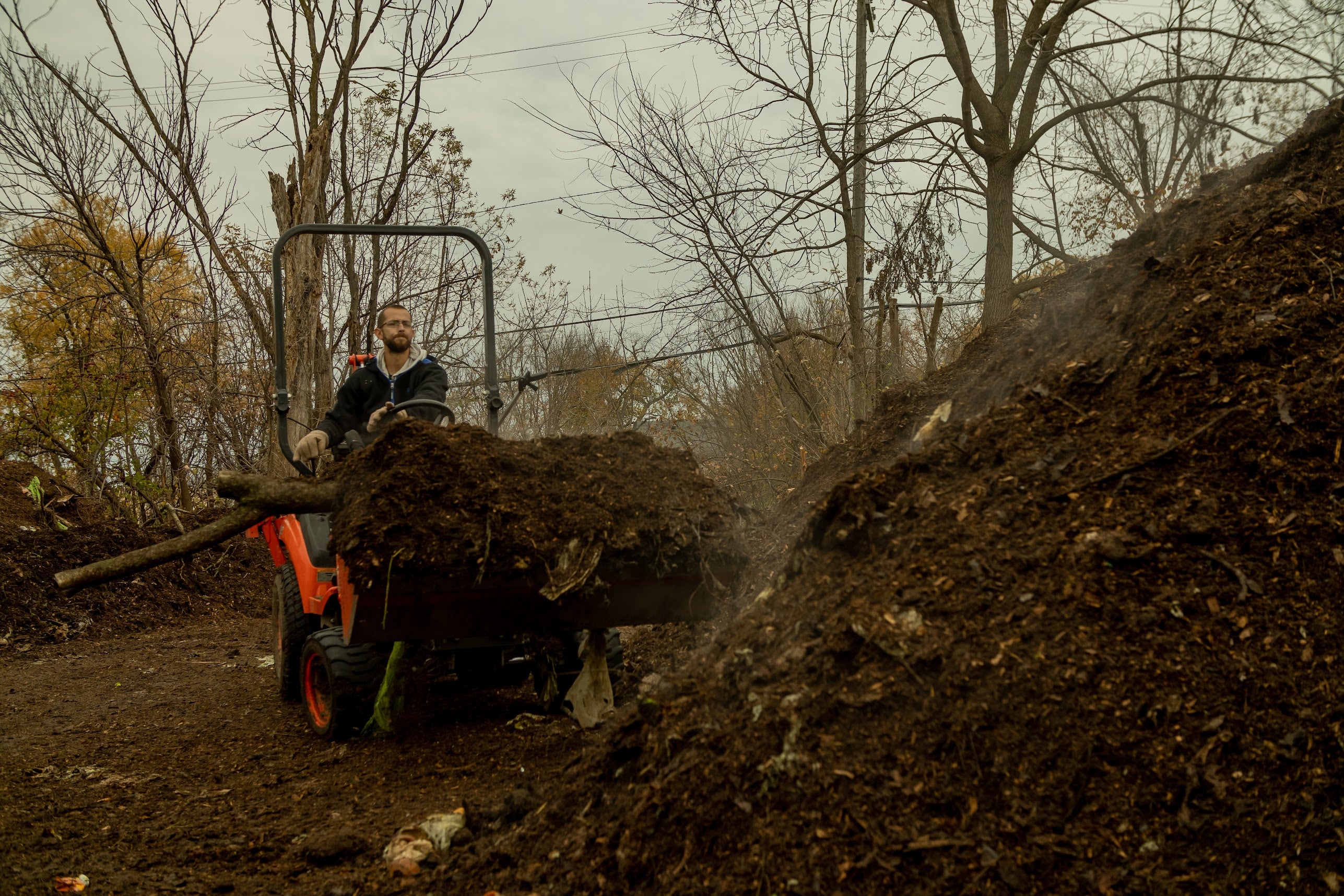 A person moving steaming piles of compost on a tractor