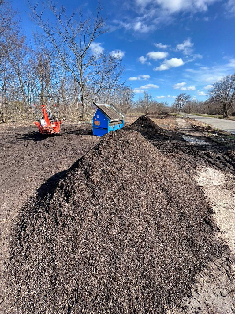 A large pile of finished compost with a tractor and compost screener in the background